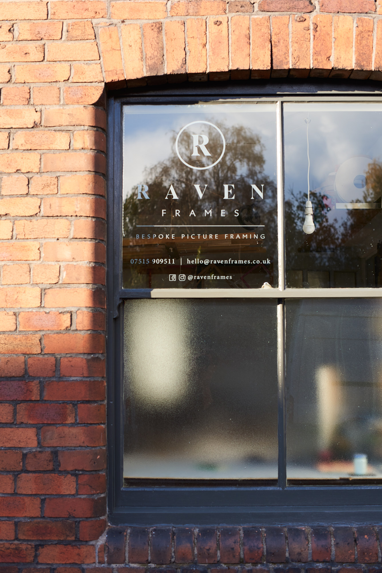 Photograph of red brick wall and grey sash window with edged logo on glass