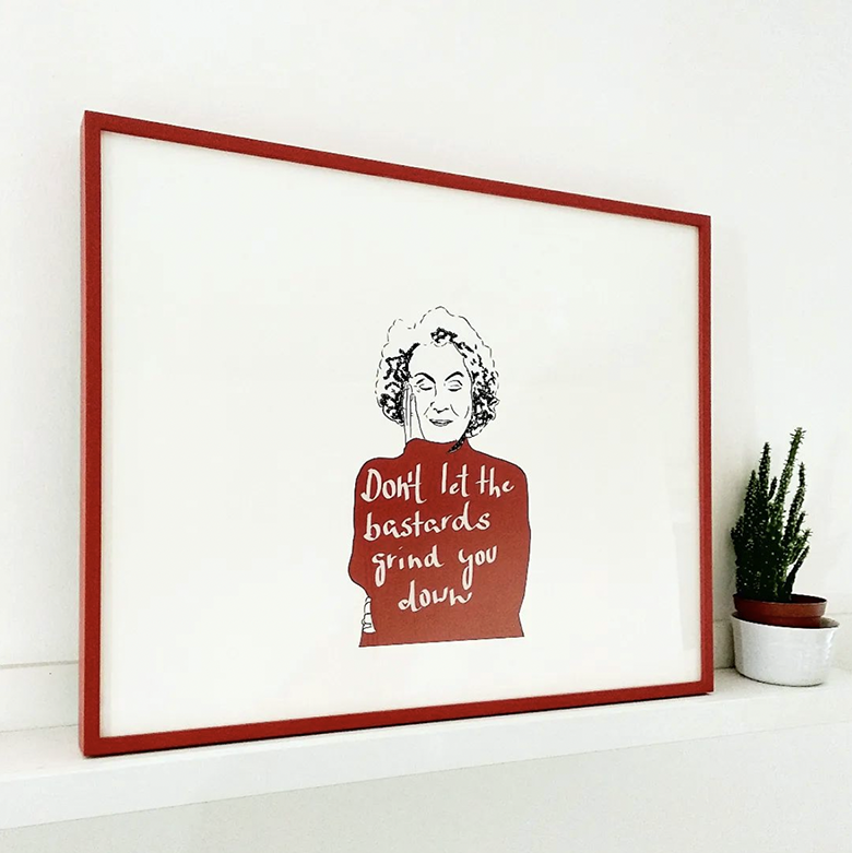 print of a woman, on whose jumper reads the slogan 'don't let the bastards grind you down' framed in slim red painted frame