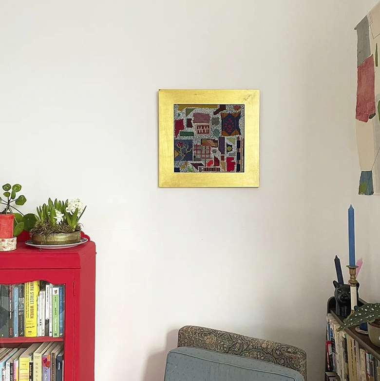 gold leaf-framed abstract tapestry, mounted on a wall above a red bookshelf