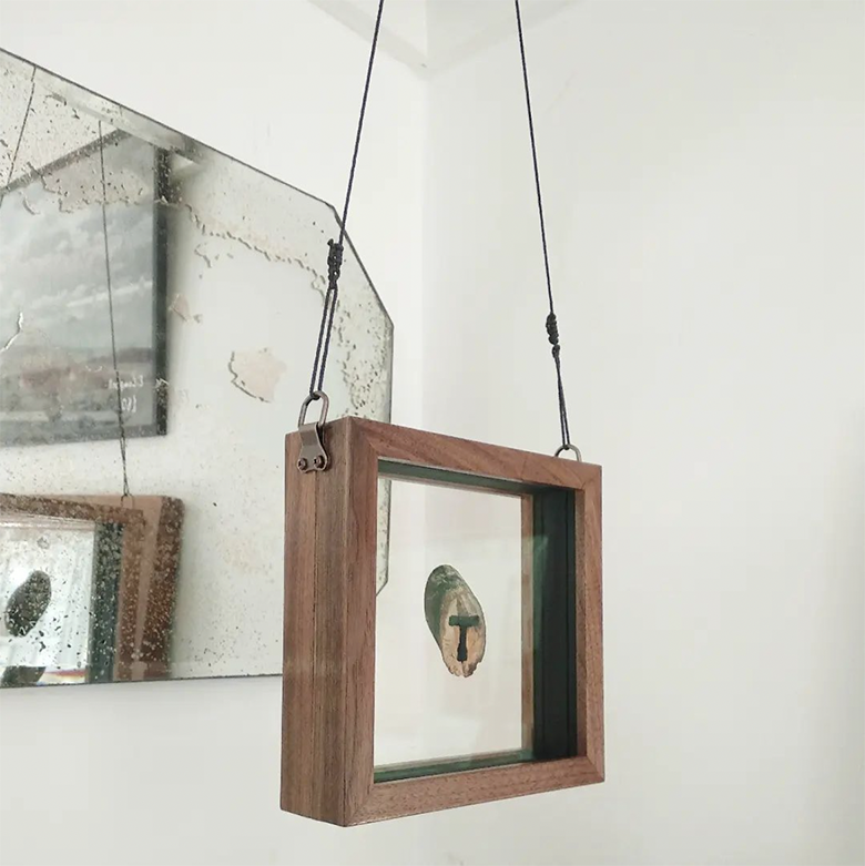 artefact hanging from wires with mirror in background framed in double walnut frame