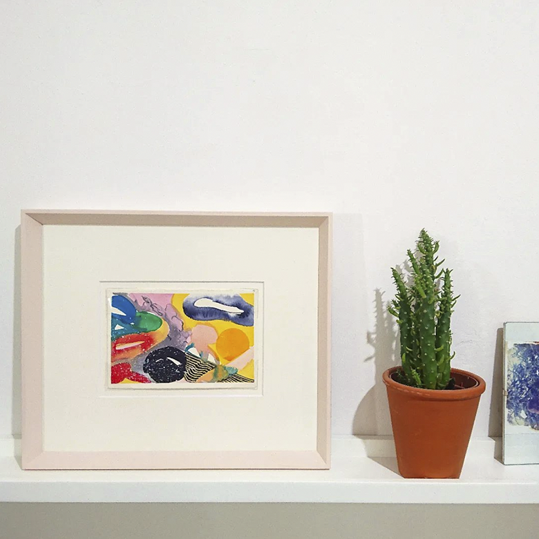 multicolour, abstract painting framed in pale pink bevelled frame beside potted cactus