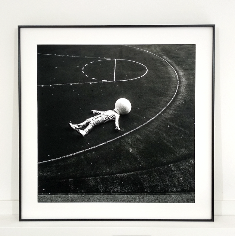 photo of a doll like an alien on a floor with basketball court-style markings in slimline black aluminium frame