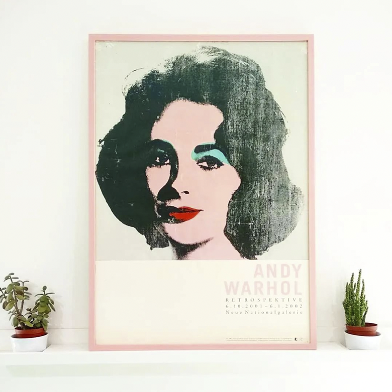 Andy Warhol posting depicting painting of a woman with dark hair and scarlet lips framed in slim light pink frame